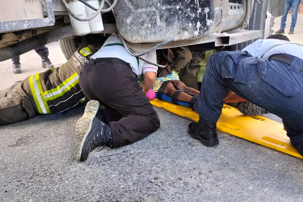 Paramedics and firefighters attend to a cyclist trapped under a dump truck at a gas station intersection in Cancún