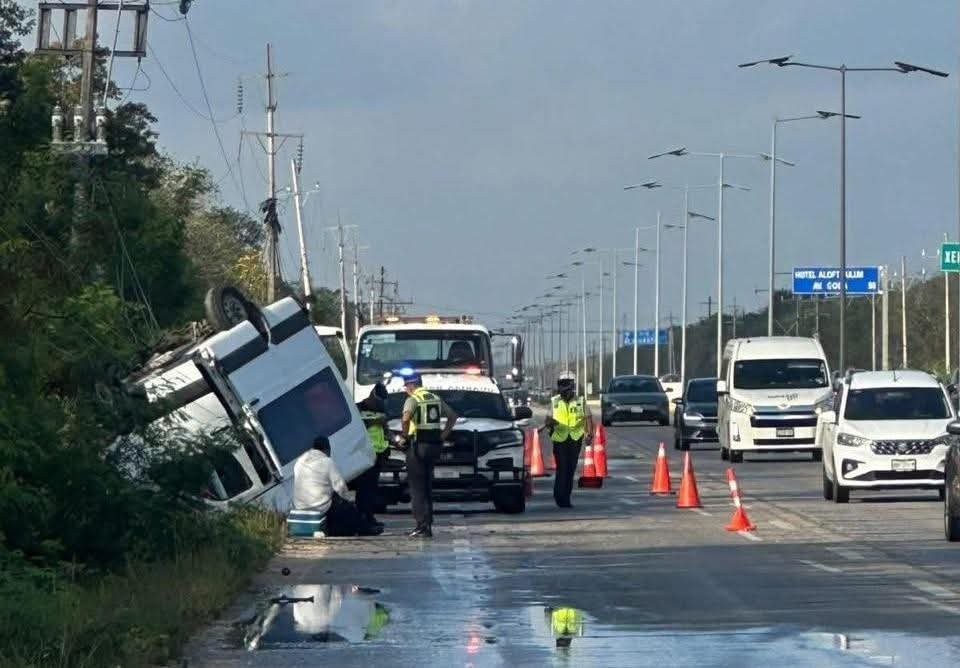A truck overturned on the side of the highway with emergency responders at the scene and vehicles passing by.