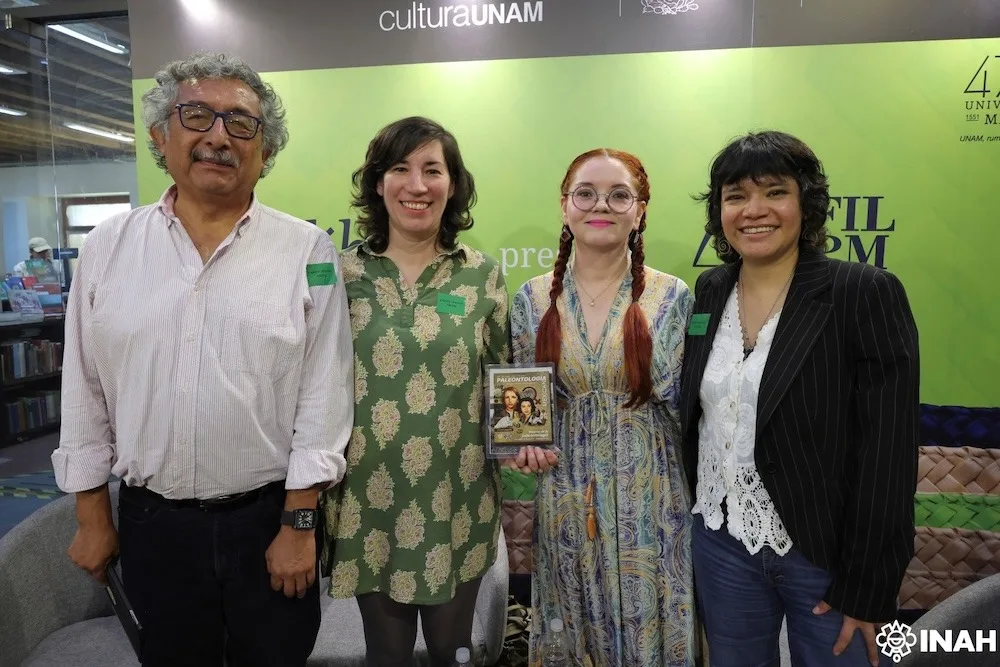 Group photo of four individuals at a UNAM event, showcasing a book titled "Paleontología"