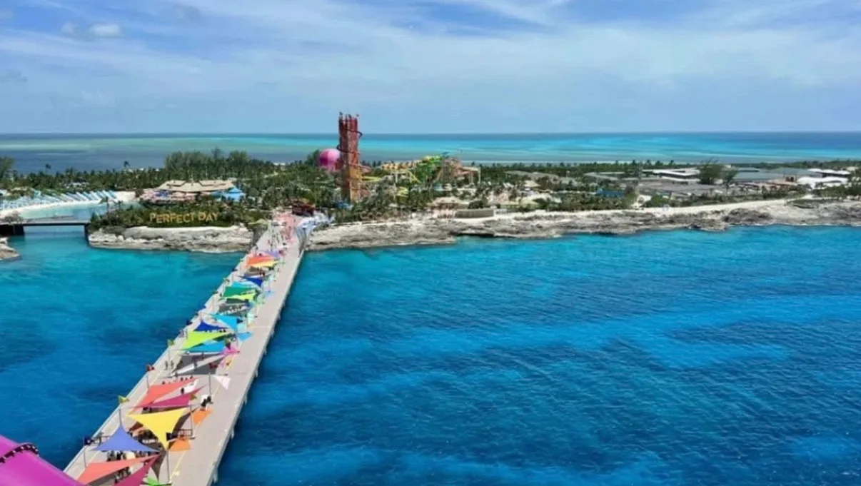 A colorful pier leading into clear blue waters at a tropical beach resort, with attractions visible in the background.$# CAPTION