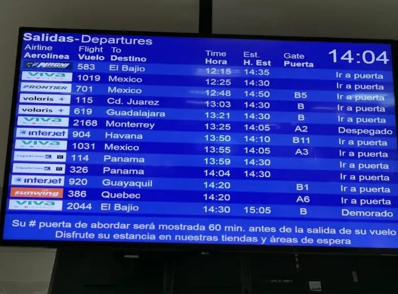 Passengers waiting at Cancún International Airport terminal with flight information boards visible