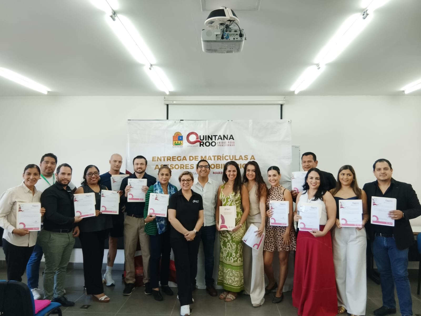 A group of individuals holding certificates at a certification ceremony in Quintana Roo, with a banner in the background.$#$ CAPTION