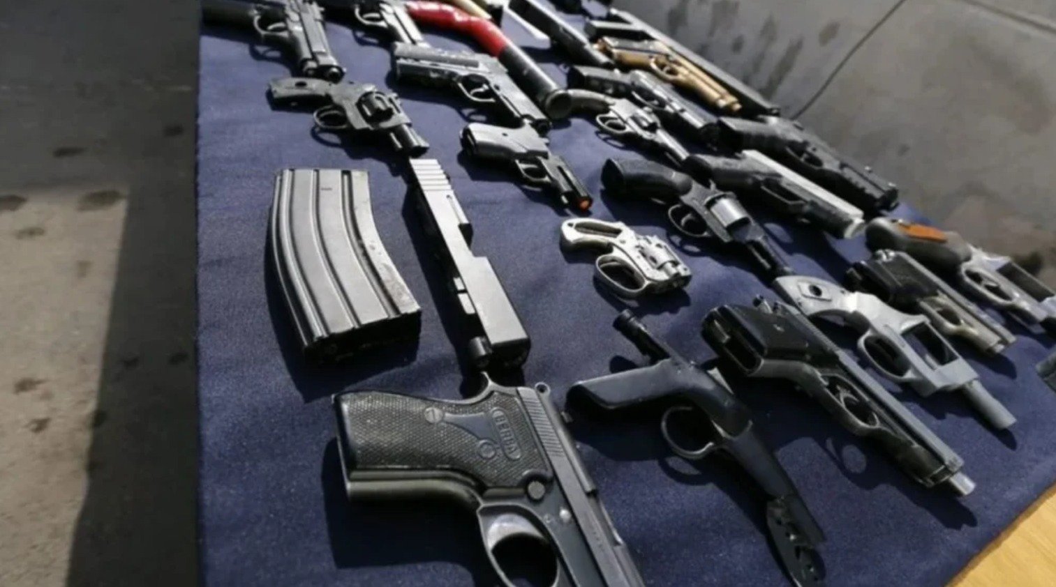 A variety of handguns and firearms arranged on a blue tablecloth for display.$# CAPTION