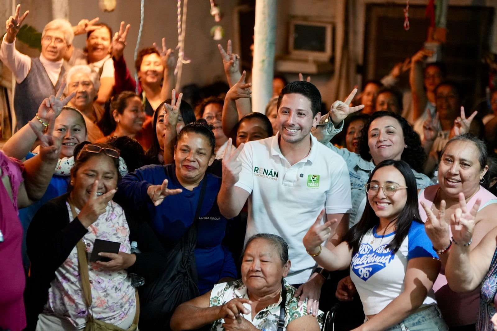 A joyful gathering of women and a man smiling and giving peace signs, showcasing unity and happiness in a community event.$#$ CAPTION