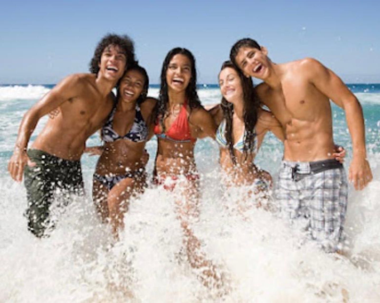 A group of five friends playing in the waves at the beach, smiling and having fun in the sun.$# CAPTION