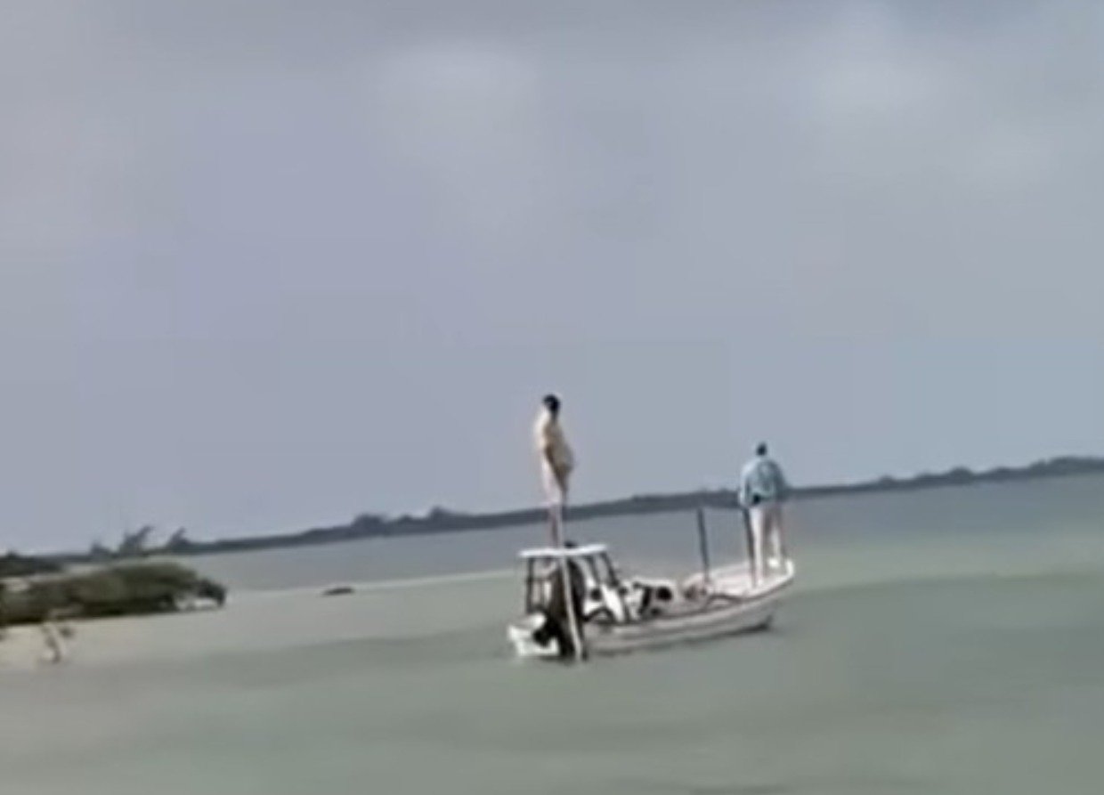 A small boat on calm water with two individuals, one standing on the bow and another at the stern, against a cloudy sky.$# CAPTION