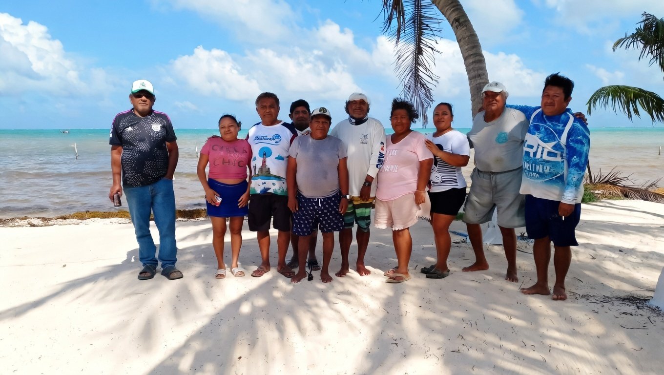A group of people standing together on a sandy beach with palm trees and a blue ocean in the background.$# CAPTION