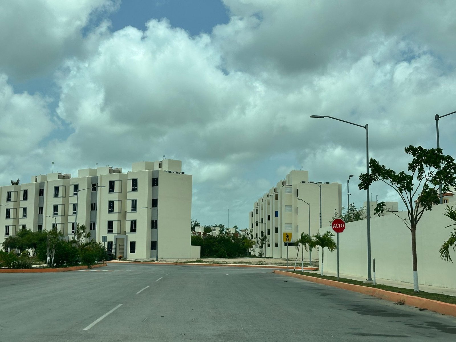 A view of a modern residential complex with multiple buildings against a backdrop of cloudy skies. A stop sign is visible in the foreground.