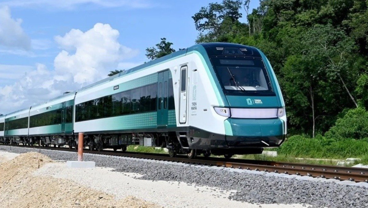 A modern green and white train traveling on a railway track surrounded by lush greenery and blue skies.