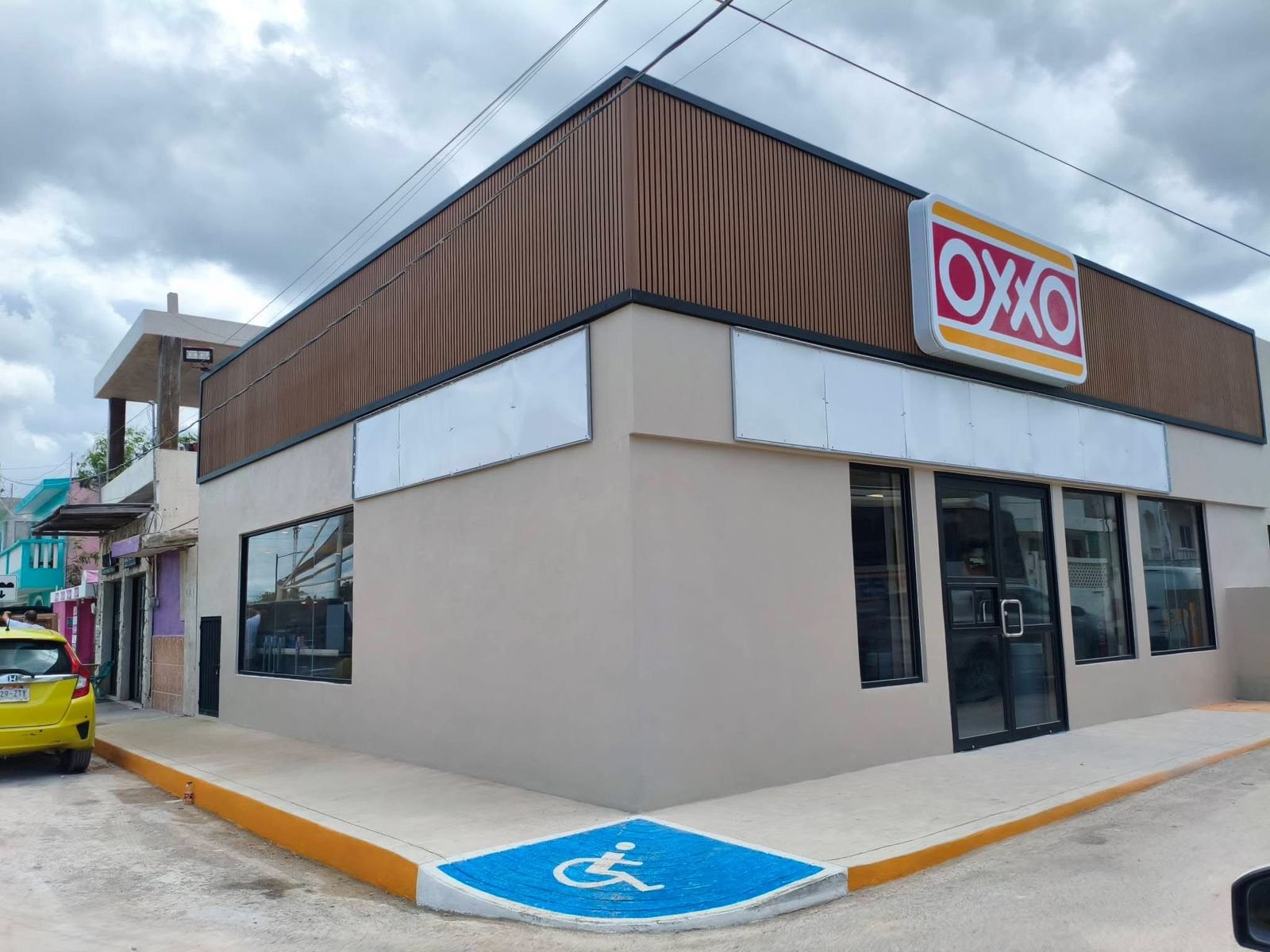 Exterior view of a new OXXO store with a yellow car parked nearby and a handicapped parking space visible