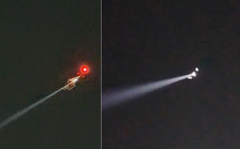 A helicopter with a red light and a search beam flying in the night sky