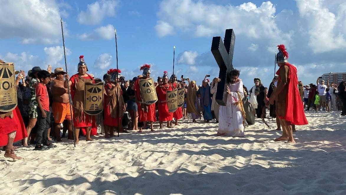 A reenactment of a biblical scene on the beach with characters in historical costumes, including Roman soldiers and a figure carrying a cross, surrounded by spectators.$#$ CAPTION