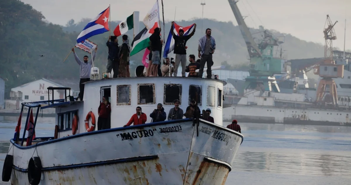A group of people waving flags stands on the deck of a boat, with various boats and cranes in the background.$# CAPTION