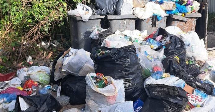 Piles of garbage including glass bottles, cans, and plastic bags scattered at the entrance to Playa Mia beach in Cozumel