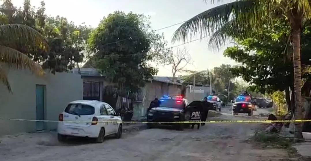 A street scene showing police vehicles with lights flashing, along with a marked police car, surrounded by caution tape in a quiet neighborhood. A palm tree is visible on the left.