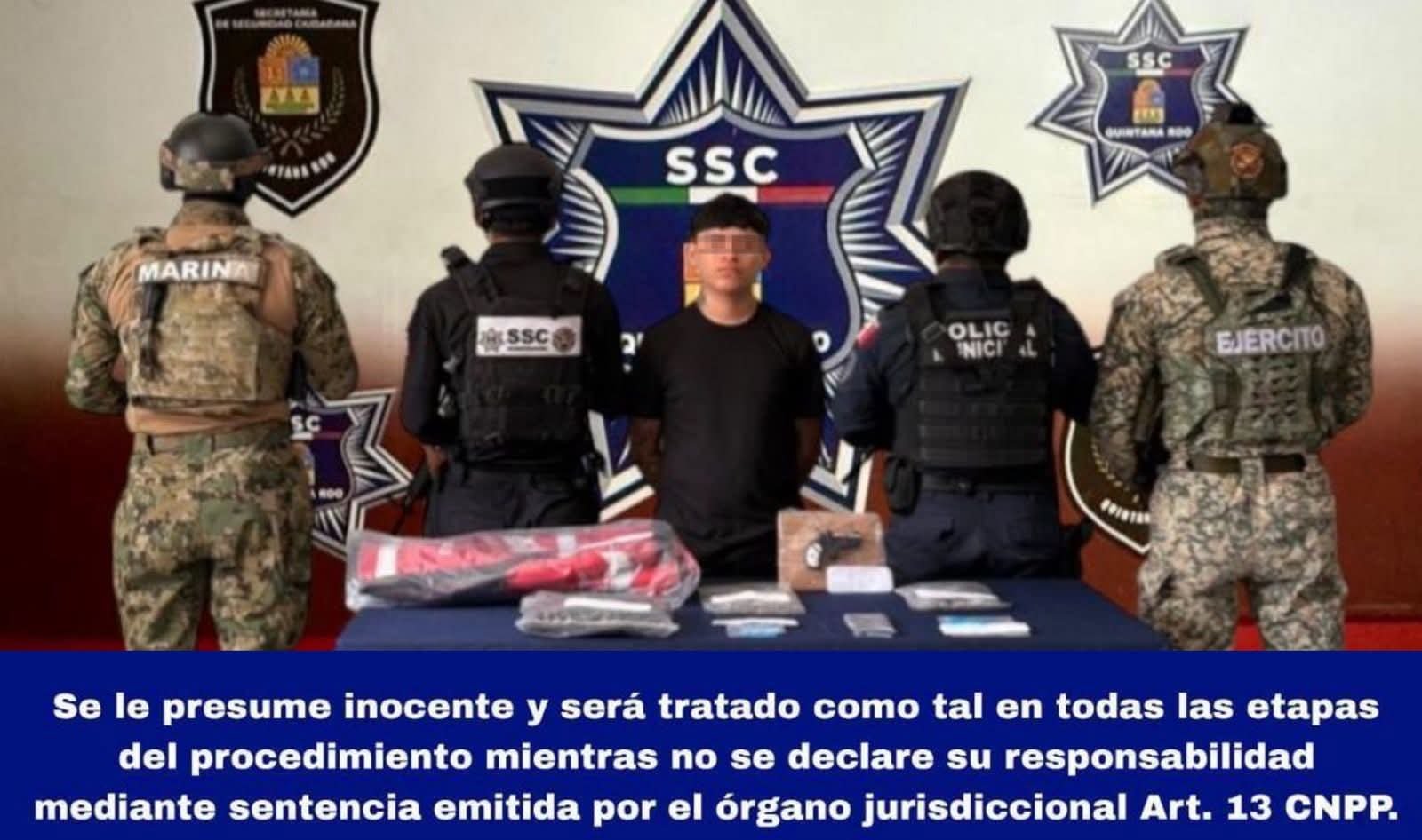 A police operation featuring officers in tactical gear and a detained individual standing in front of a law enforcement emblem, with items displayed on a table.$# CAPTION