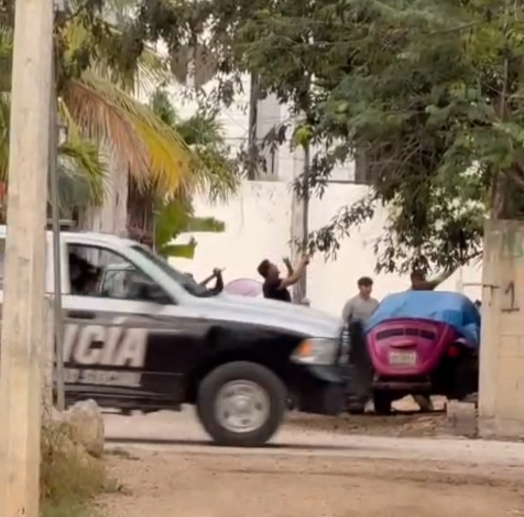 A police vehicle drives past while individuals interact near parked cars in an urban setting.$#$ CAPTION