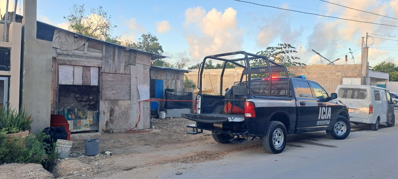 A police truck parked on a street in front of a makeshift wooden structure with various items scattered around.$# CAPTION