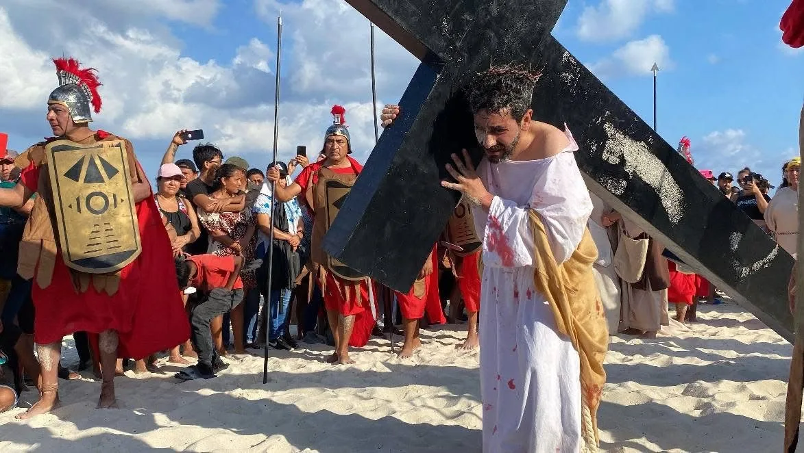 Rafael Pérez Pasquel carrying a large wooden cross on Playa Delfines beach during the Passion Play