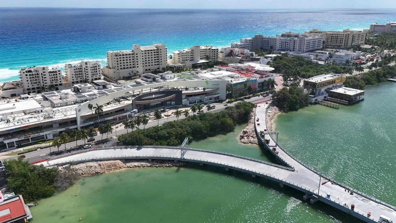 Aerial view of Cancun, showcasing coastal buildings and a connecting bridge over a body of water with the ocean in the background.$# CAPTION
