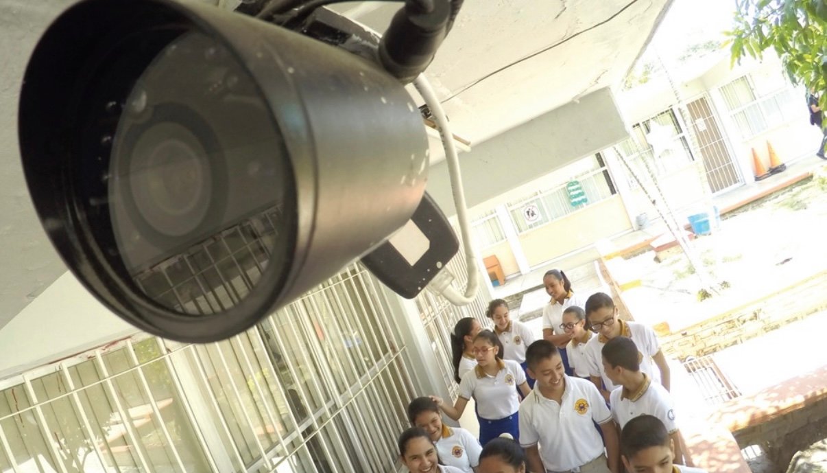 A security camera mounted above a group of students walking in a school corridor.$# CAPTION
