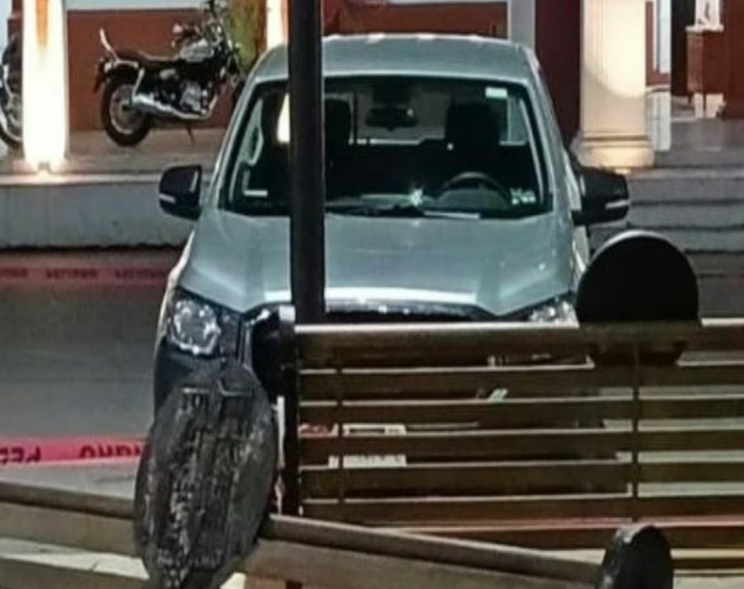 A silver vehicle is parked in front of a wooden bench with a motorcycle visible in the background, and caution tape on the ground.$# CAPTION