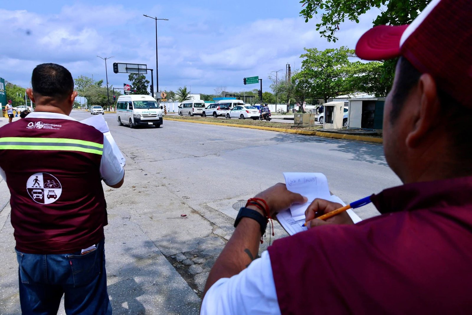 Two traffic officials observing and taking notes on vehicles on a road.$# CAPTION