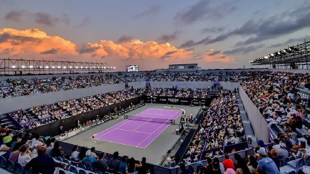 A bustling tennis stadium filled with spectators under a colorful sky at sunset, featuring a purple tennis court.$# CAPTION