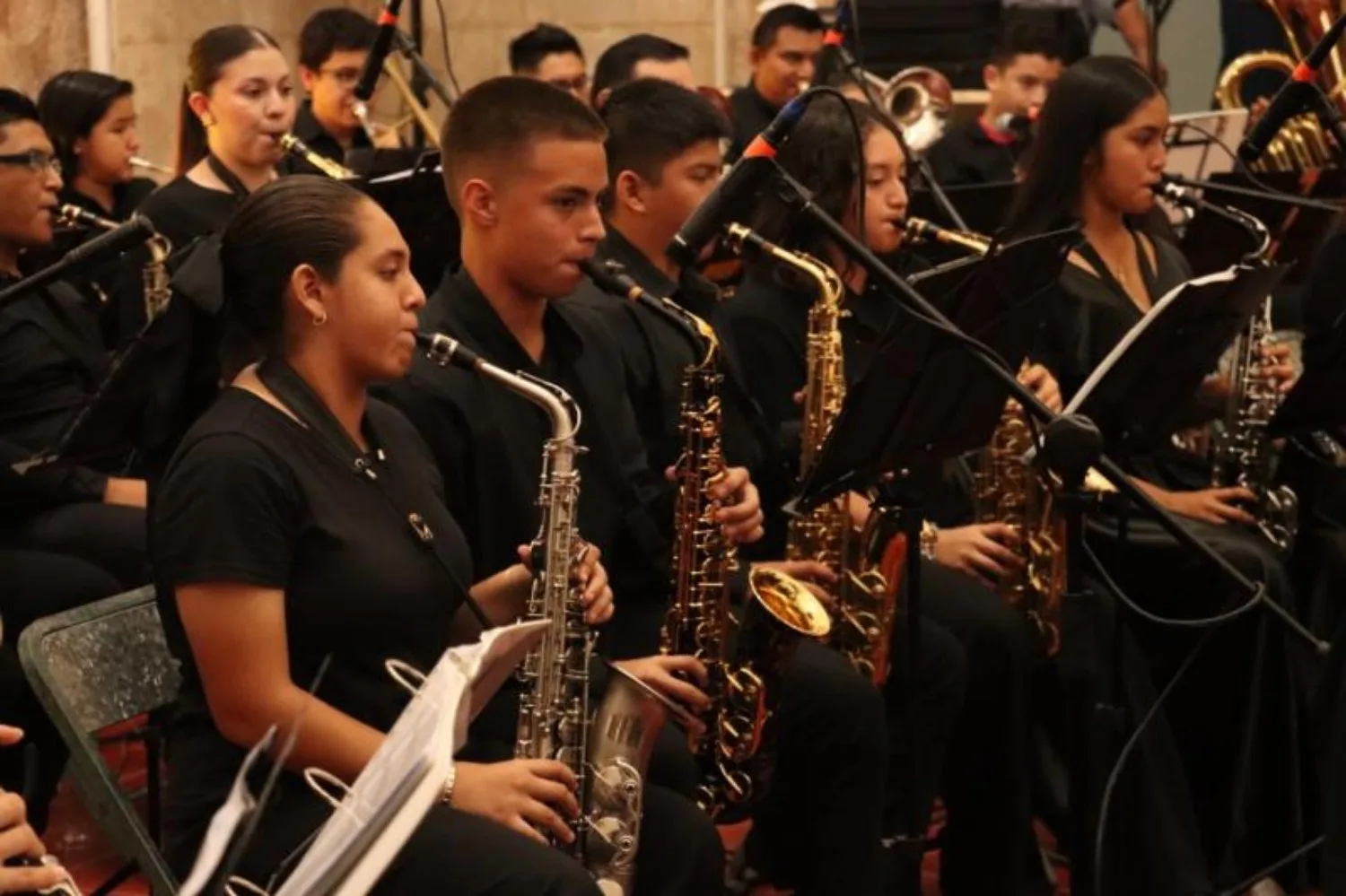 A group of young musicians playing saxophones and other instruments in a concert setting.$# CAPTION