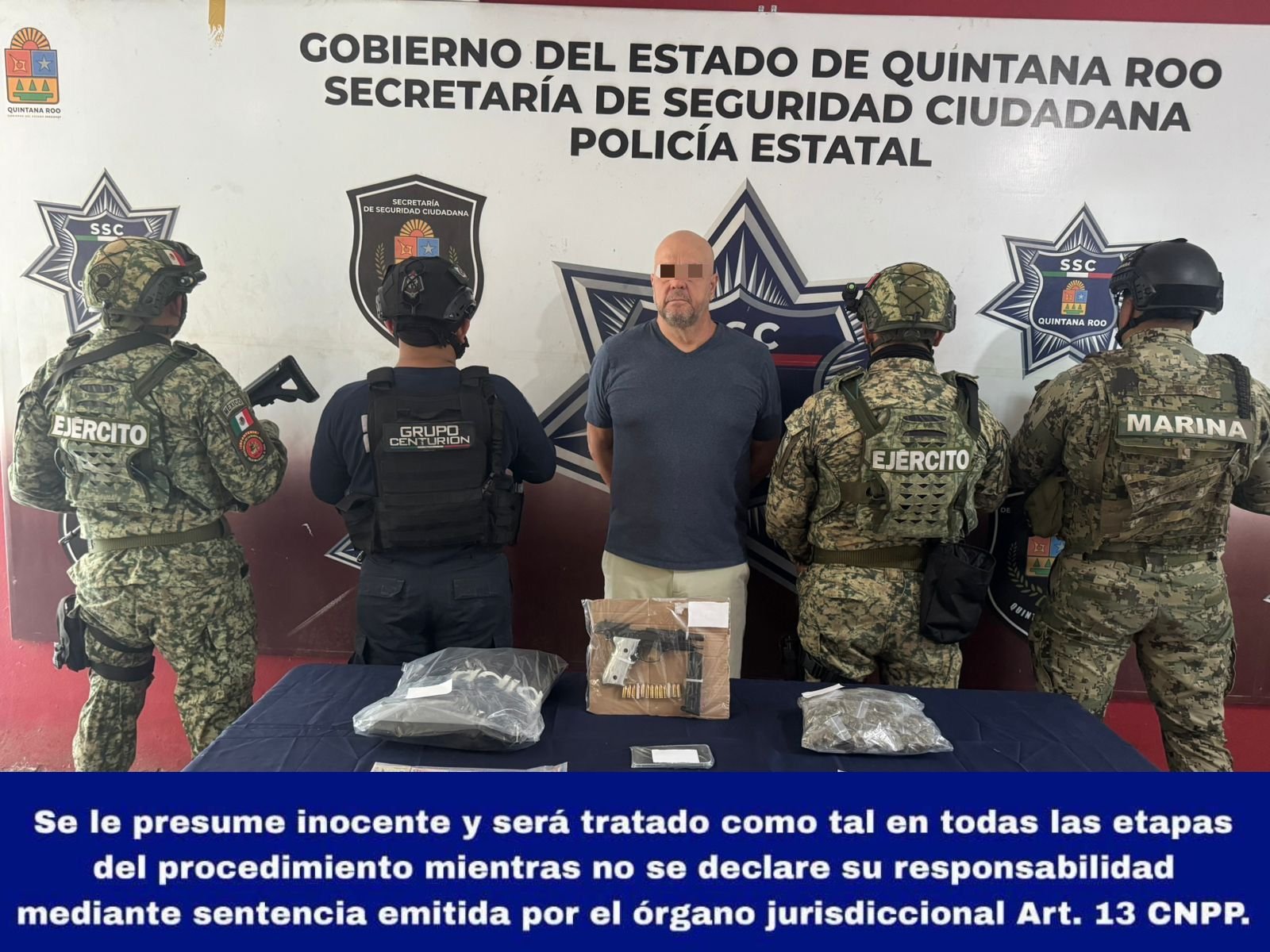 A man stands in front of law enforcement officers and a table displaying confiscated items in Quintana Roo, Mexico.$# CAPTION