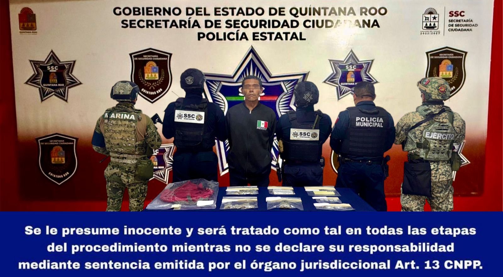 Law enforcement officers stand around an apprehended individual in front of a governmental backdrop, with evidence displayed on a table in front of them.$# CAPTION