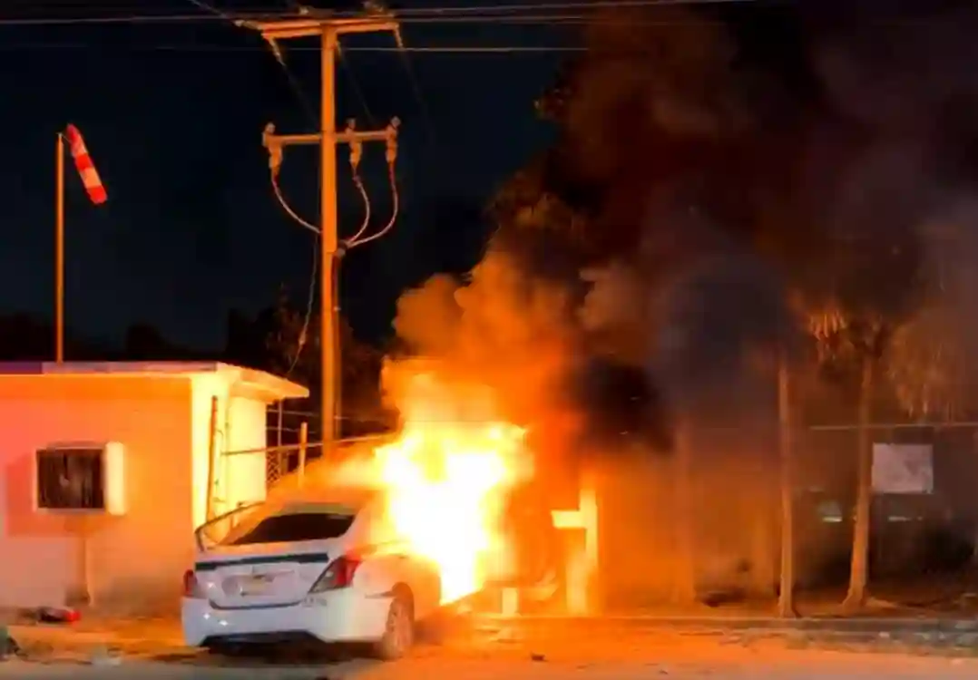 A taxi engulfed in flames after crashing into a water utility property in Cancún following an armed attack