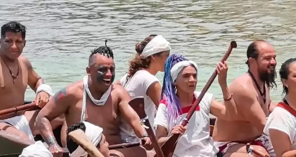 Canoeists in traditional white clothing preparing wooden canoes on a beach at dawn for the Travesía con Corazón 360 crossing