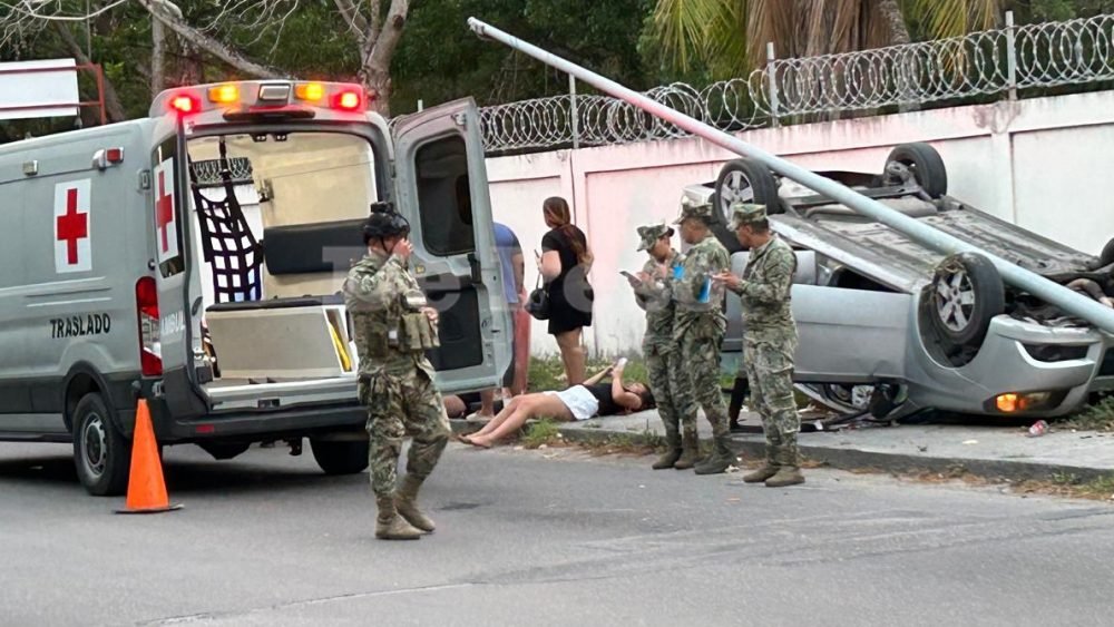 A silver Chevrolet overturned on a Chetumal street, with its wheels up and emergency personnel nearby.