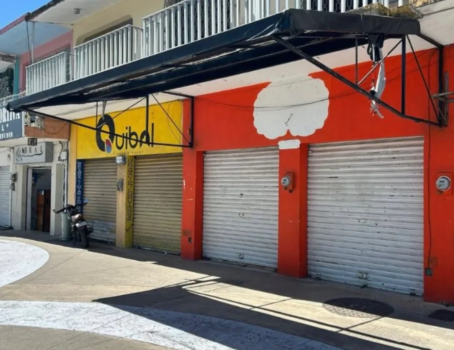 A row of closed storefronts with colorful signage and metal shutters in a street setting.$# CAPTION