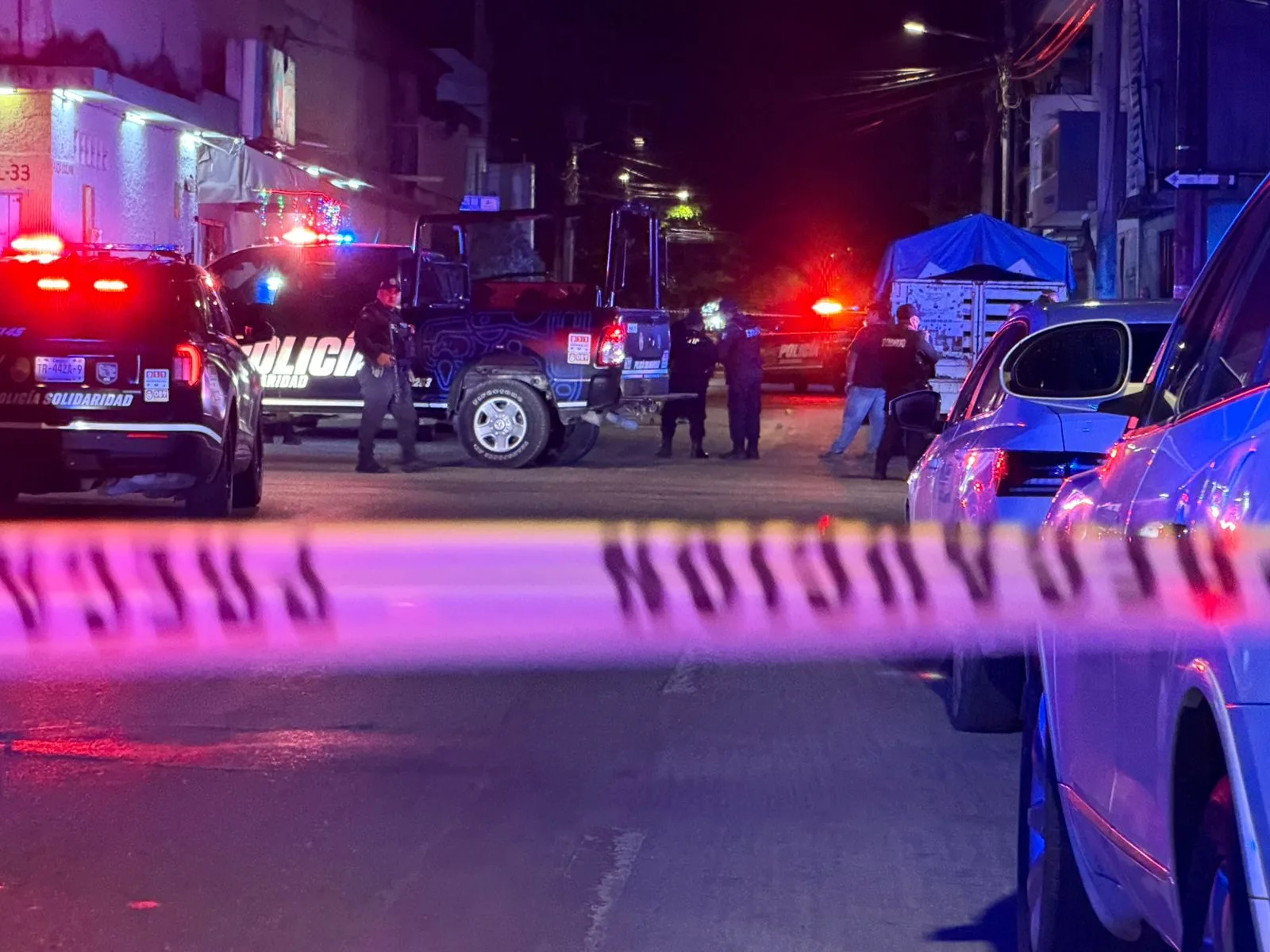 A white Toyota Hilux pickup truck with multiple bullet holes in its side, parked on a street in Playa del Carmen.