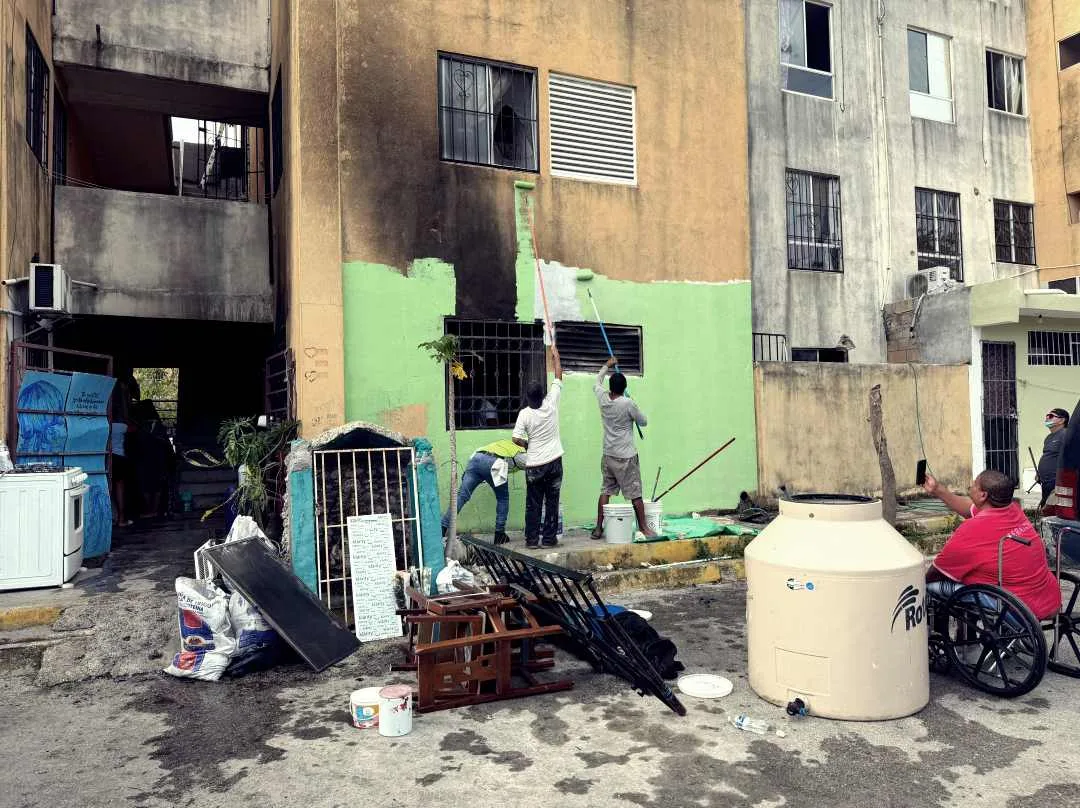 Neighbors cleaning and painting a fire-damaged apartment in Cancún's Paseos del Mar neighborhood
