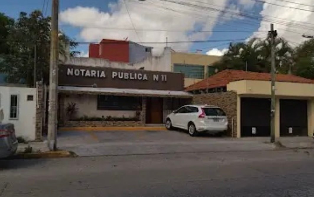 Exterior view of a public notary office with a car parked in front and clear skies above.$# CAPTION