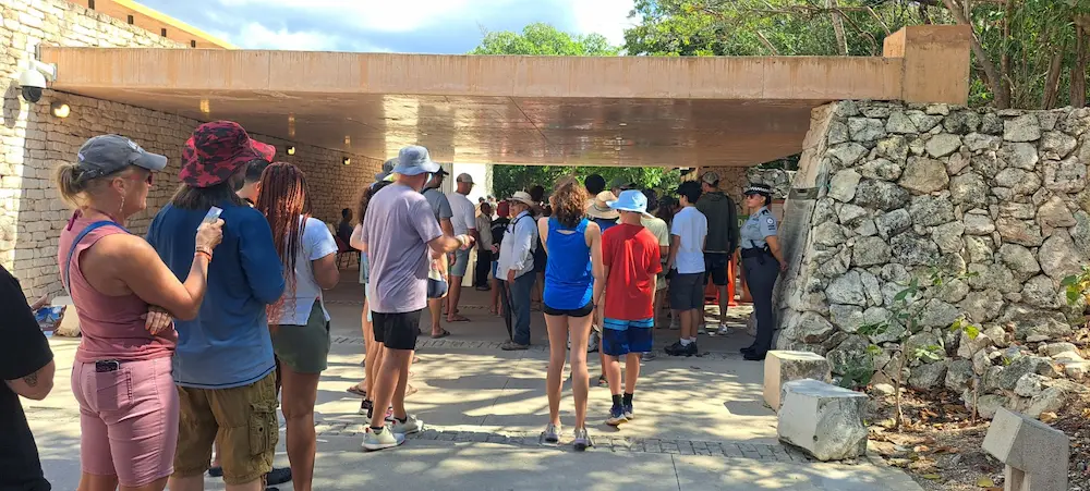 Tourists waiting in line at the entrance of Tulum archaeological zone with security personnel and metal detectors visible