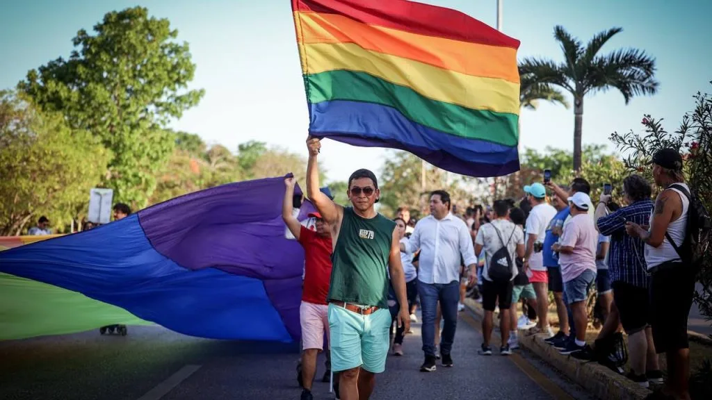 People marching with rainbow flags at a Pride event in Cancun