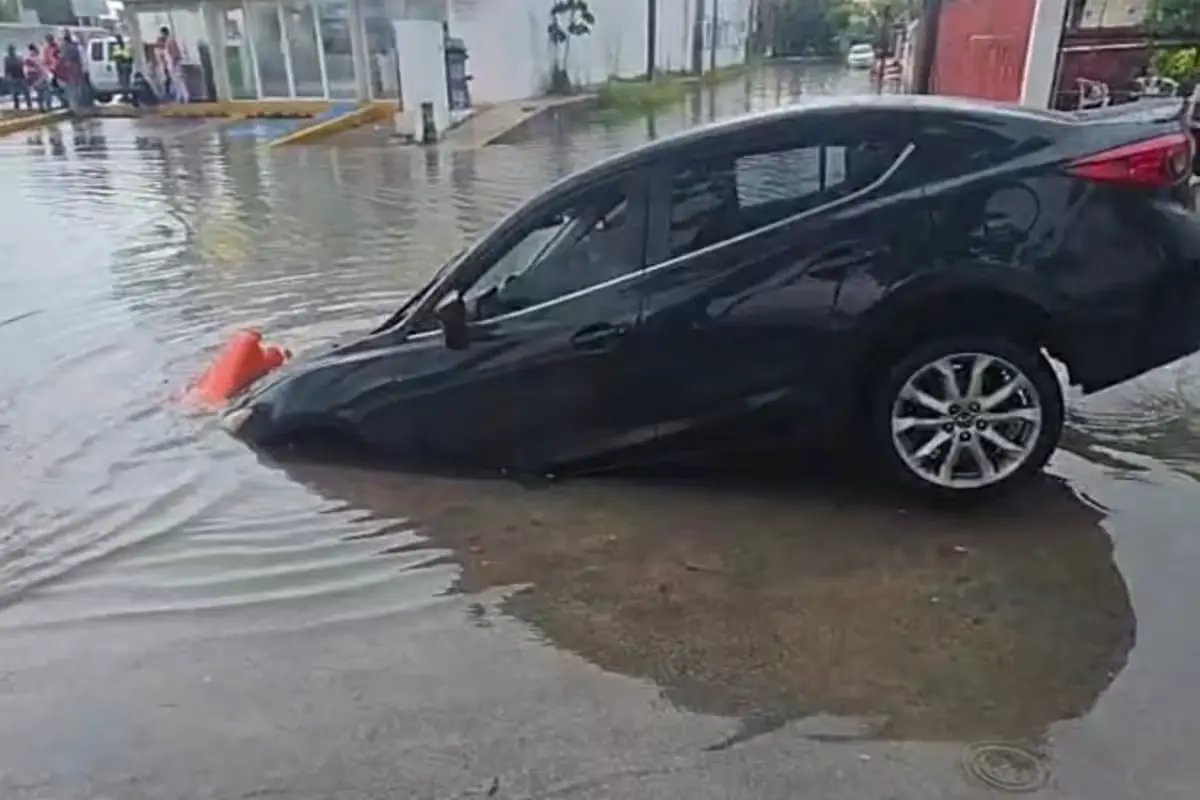 A black Mazda partially submerged in a water-filled trench on Benito Juarez Avenue in Chetumal