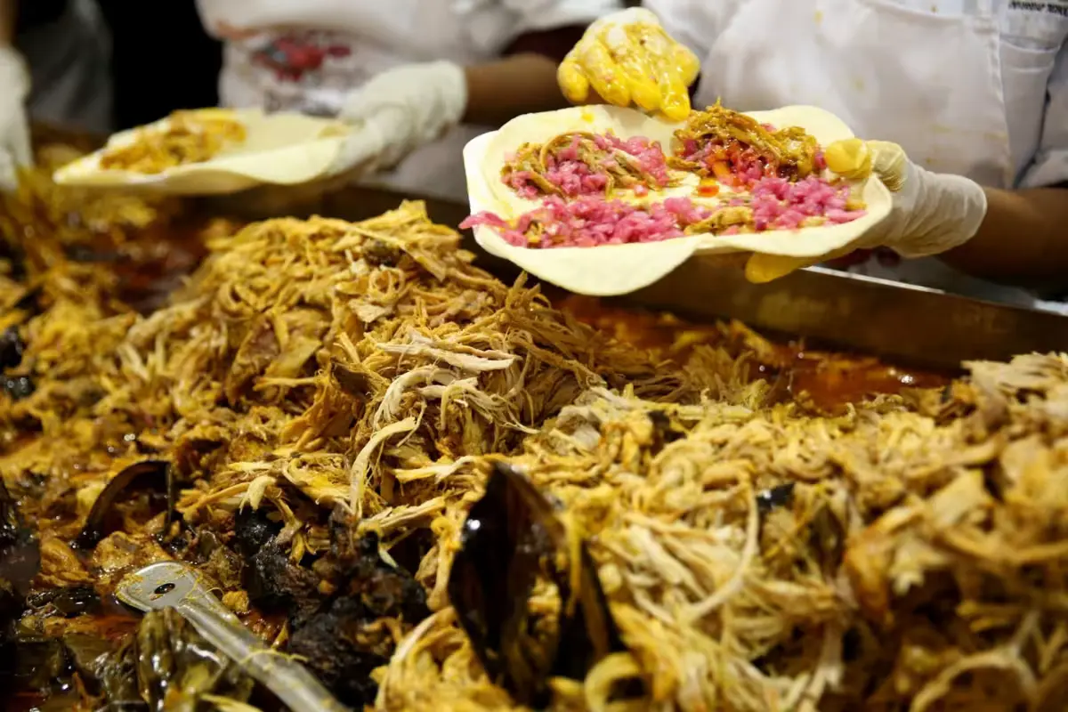 A plate of cochinita pibil served with tortillas, pickled red onion, and habanero chili