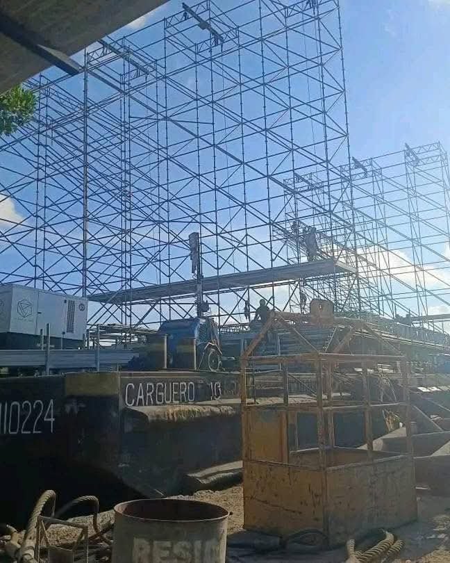 A metal stage structure on a floating platform on Nichupté Lagoon, with the new bridge in the background