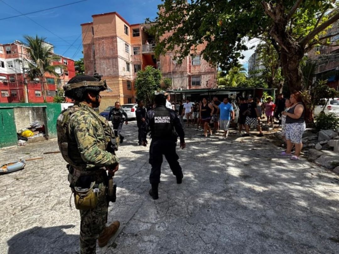 Police officers detain two suspects on a street in Cancun's Corales neighborhood as residents gather nearby