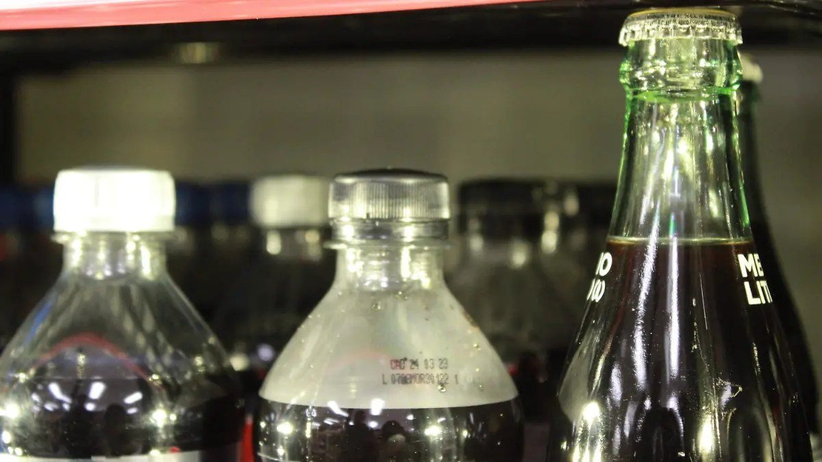 Assorted soda bottles on a table with a magnifying glass and clipboard representing a Profeco analysis
