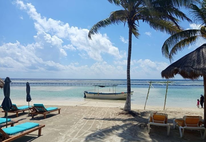 A beach in Mahahual with minimal sargassum on the sand and a containment barrier visible offshore.