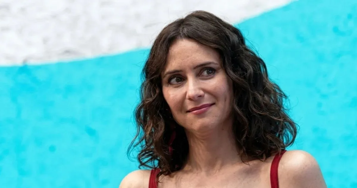 A woman with curly hair smiles softly, set against a turquoise and white backdrop that adds a vibrant touch to the image.$# CAPTION