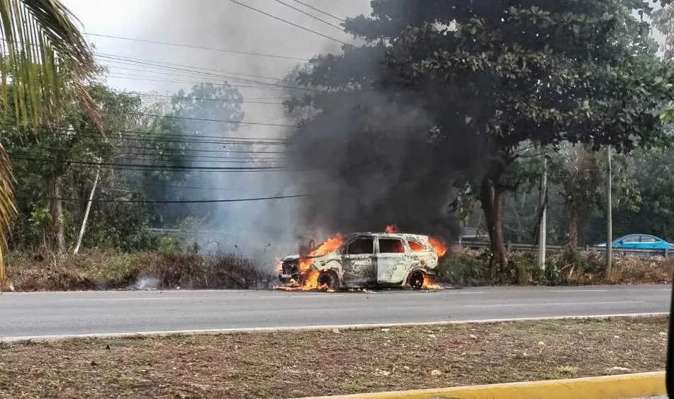 A taxi fully engulfed in flames on the side of Highway 307 near Cancun International Airport