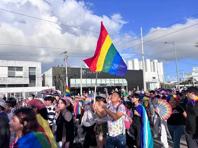 People marching in a Pride parade in Cancun holding rainbow flags
