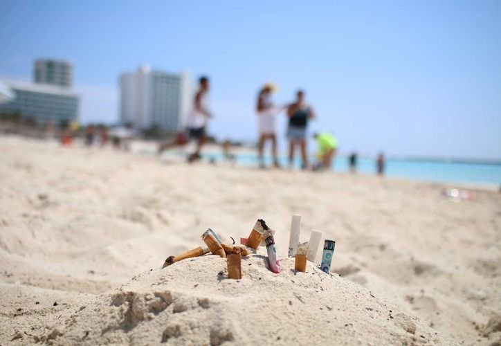 Cigarette butts scattered on a sandy beach near the ocean